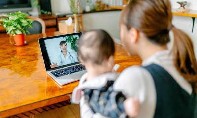 A woman holds her baby while talking to a doctor via a telehealth appointment.